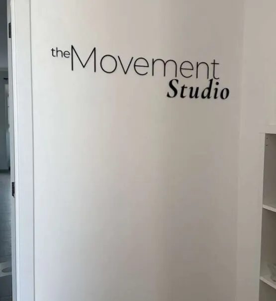 White wall with black text reading the Movement Studio near an open doorway and white shelving.